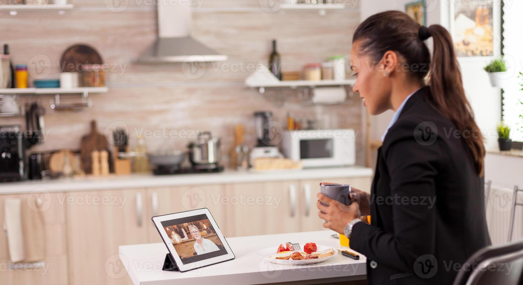 Career woman speaking with her mother on webcam during the breakfast. Using modern online internet web technology to chat via webcam videoconference app with relatives, family, friends and coworkers. photo