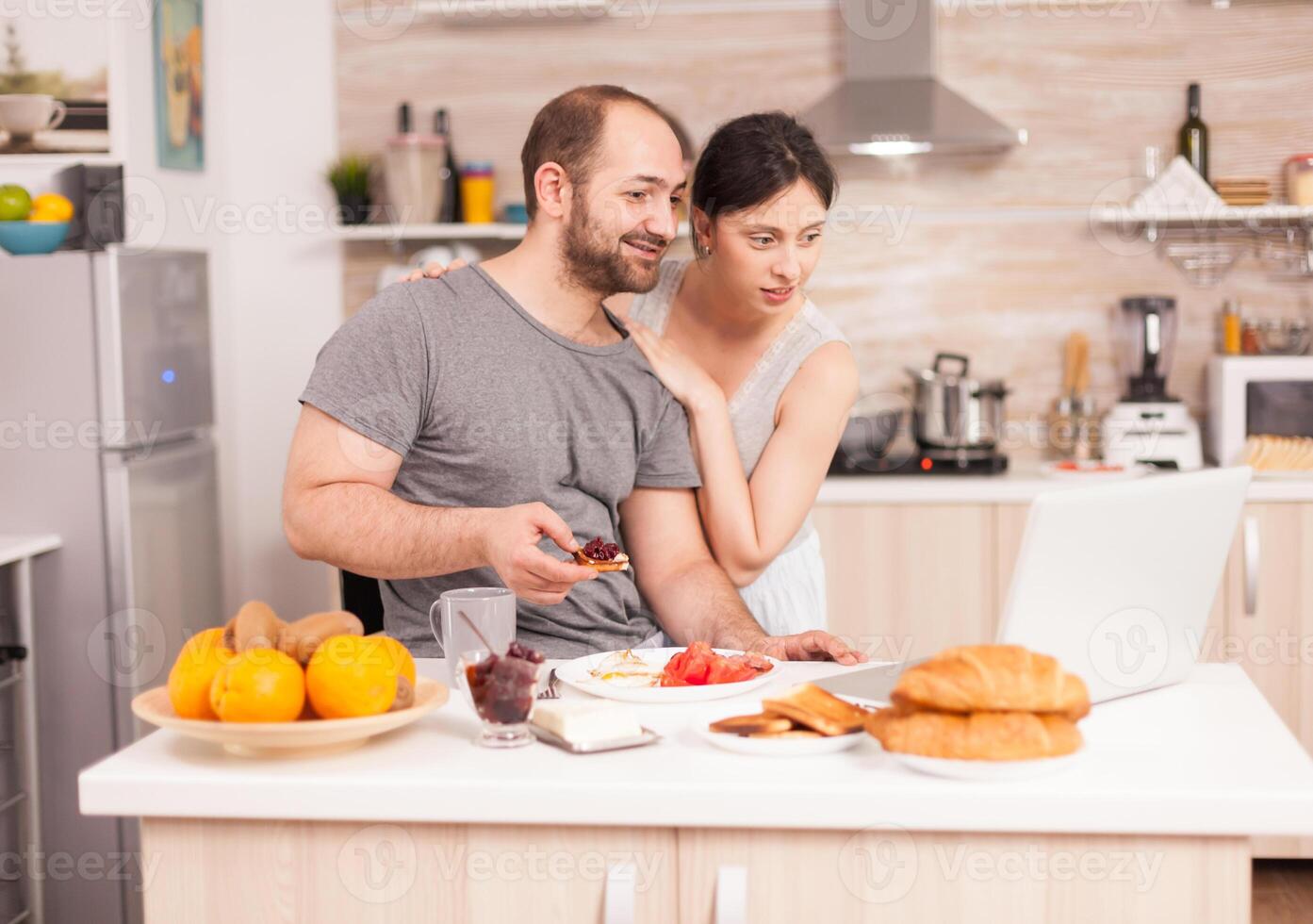 Young couple talking on video call with parents eating healthy breakfast in the morning. Videoconference in the morning, using online web internet technology, talking and communicating with relatives photo