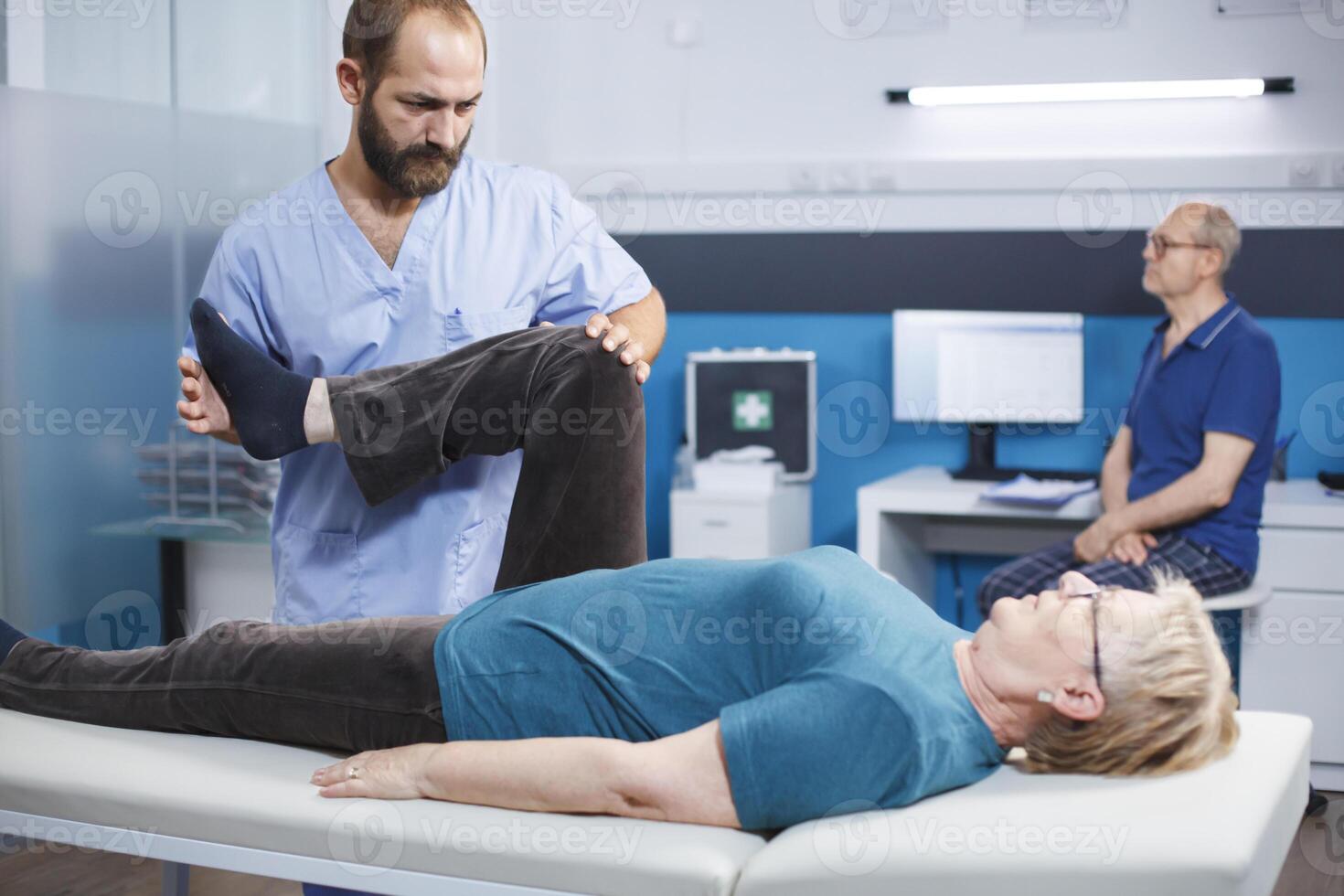 Chiropractor trying to relieve pressure from knee of old patient with arthritis and injury. Physiotherapist cracking leg bones for relief and physical recovery of senior woman with pain. photo