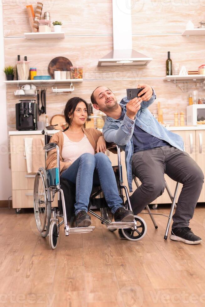 Romantic man taking selfie with disabled wife in wheelchair. Disabled paralyzed handicapped woman with walking disability integrating after an accident. photo