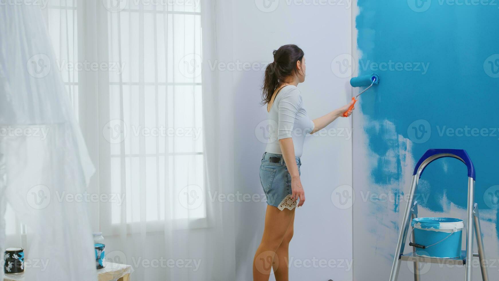 Adult woman painting wall using roller brush dipped in blue paint. Home designer renovate, renovating. Apartment redecoration and home construction while renovating and improving. Repair and decorating. photo