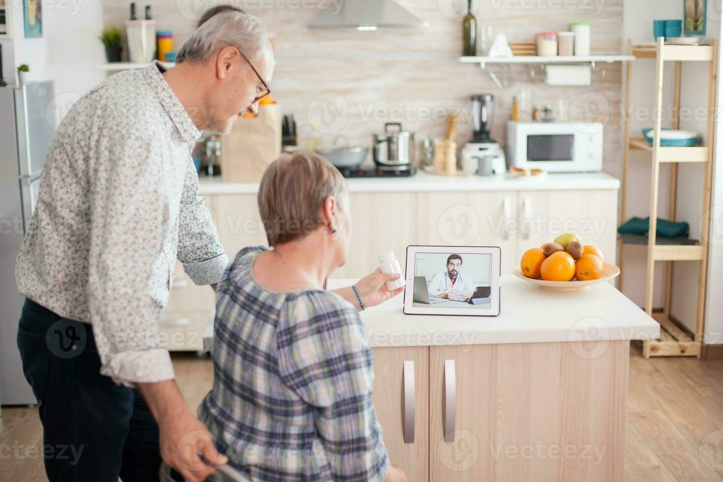 Senior couple listening doctor during telemedicine conference. Video conference with doctor using laptop in kitchen. Online health consultation for elderly people drugs ilness advice on symptoms, physician telemedicine webcam. Medical care internet chat photo