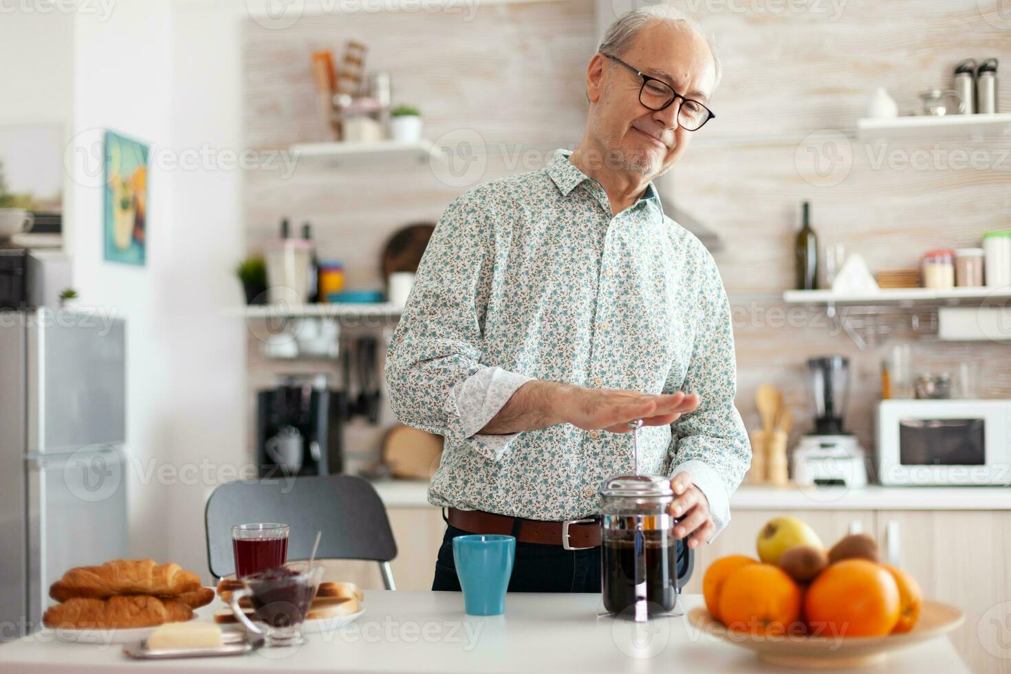 Senior man making coffee using french press during breakfast in kitchen. Elderly person in the morning enjoying fresh brown cafe espresso cup caffeine from vintage mug, filter relax refreshment photo