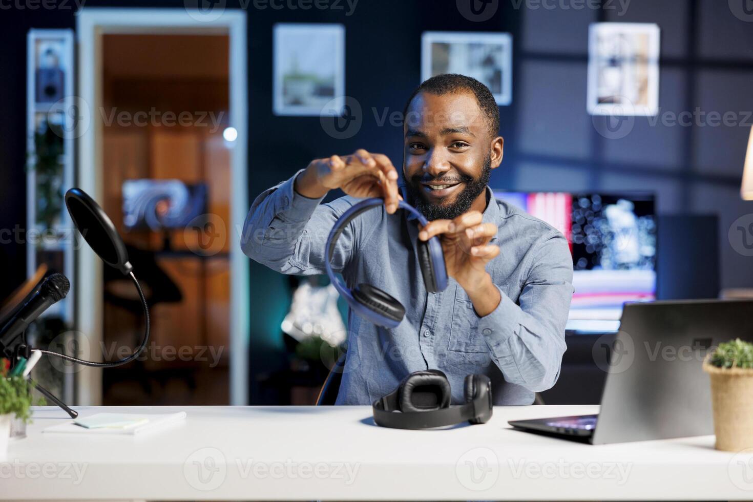 African american vlogger doing technology video vlog, showcasing newly released headphone pairs to viewers. Smiling man greeting subscribers, presenting wireless music listening gear photo