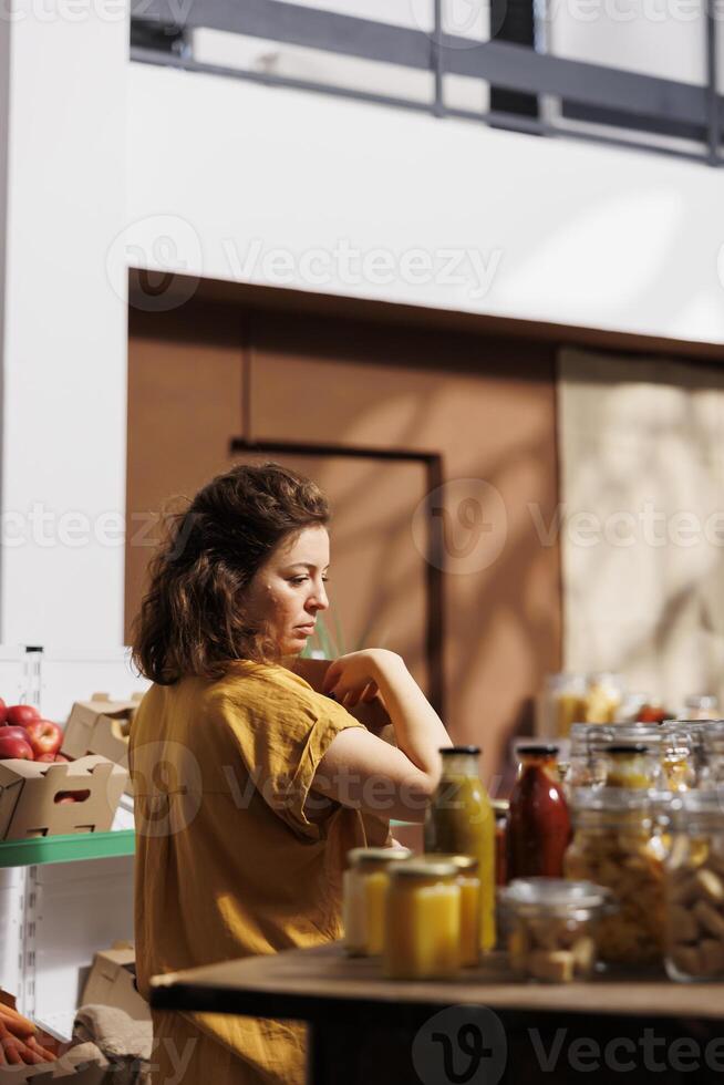 Shopper buying mindfully, picking bio produce in zero waste store using reusable compostable paper bags to minimize plastic usage. Green living customer looking for vegan pantry staples photo