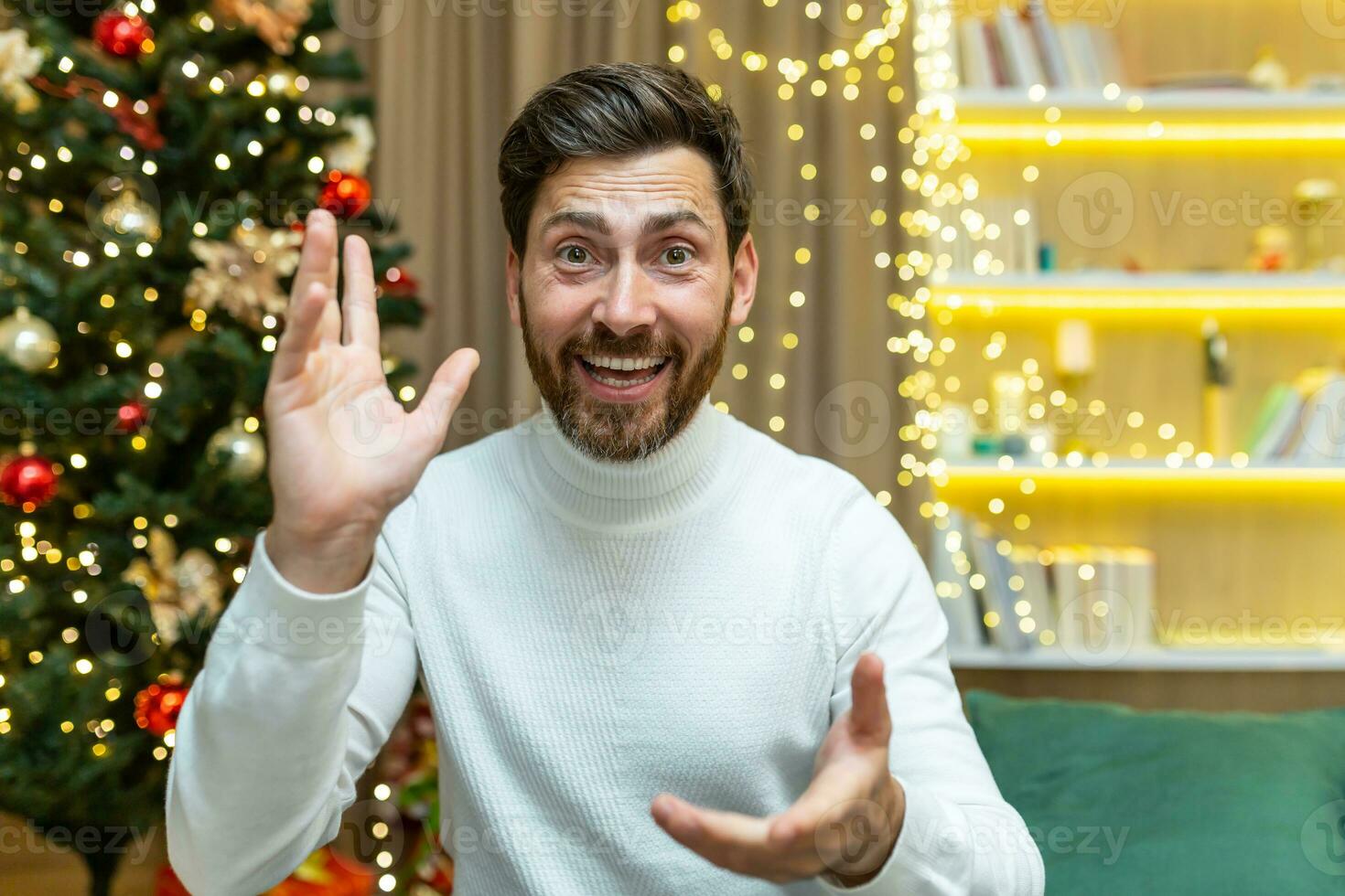 Closeup happy man talking on a video call looking web camera and talking with friends, at home for Christmas sitting on a sofa in the living room near the Christmas tree, on New Year's holidays. photo