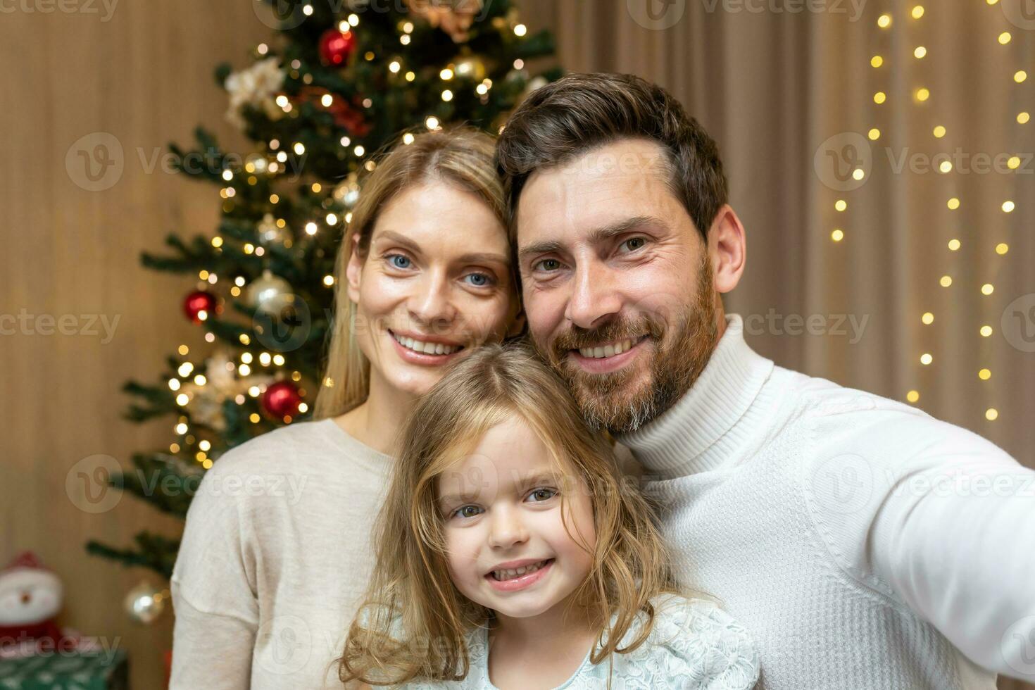 Portrait of happy family on Christmas, family man woman and daughter looking at camera and smiling, celebrating new year together at home, using phone for video call and remote communication online. photo