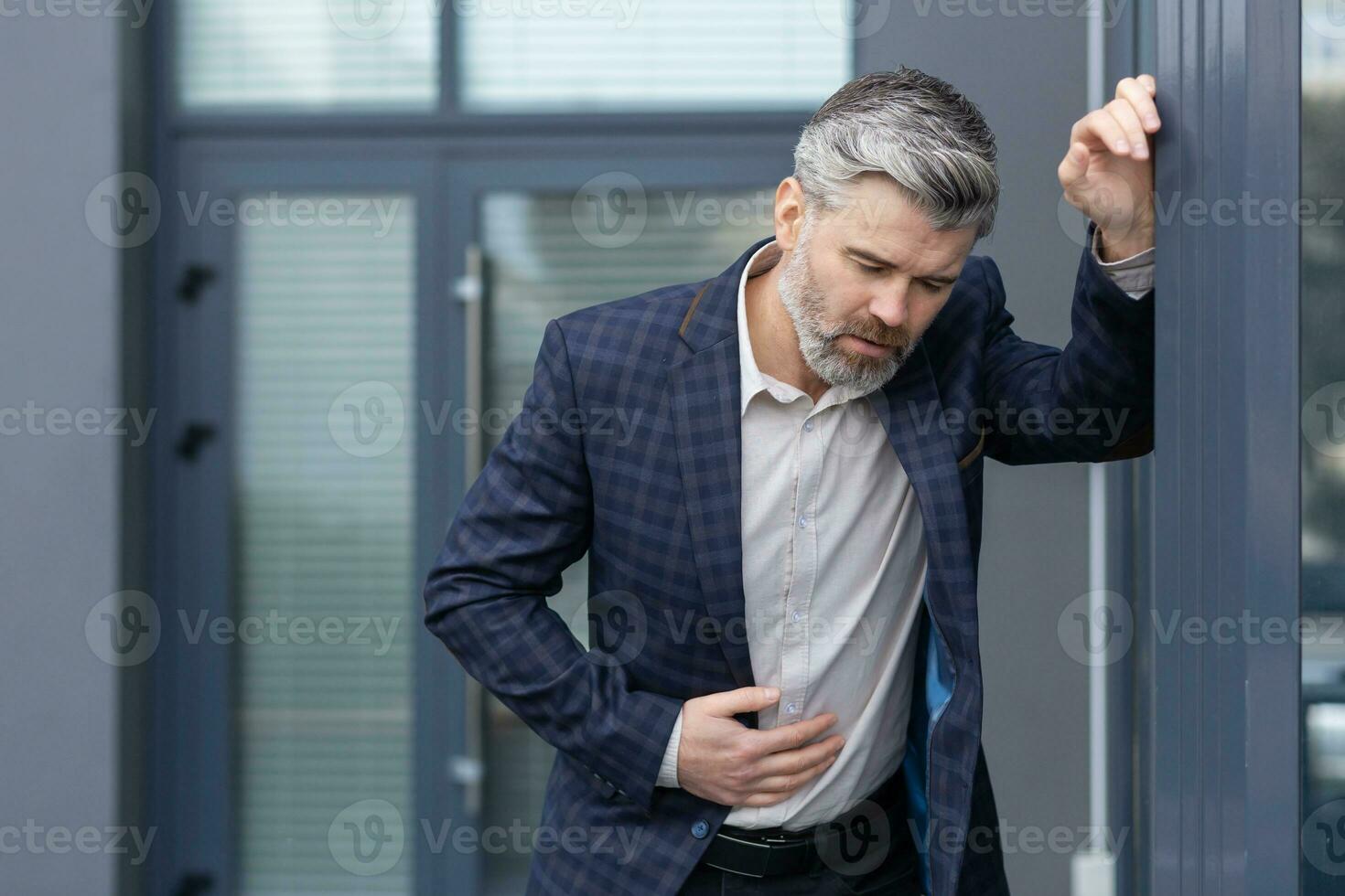 Mature gray haired boss has food poisoning, man outside office building has severe stomach pain and nausea, boss is vomiting sick. photo
