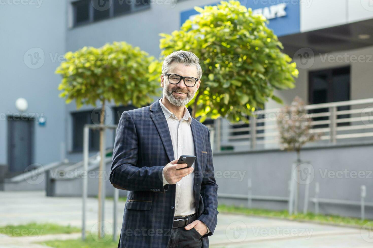 Portrait of a mature businessman, a grayhaired experienced man smiling and looking at the camera, a boss in a business suit holding a smartphone, an investor looking at the online stock exchange. photo