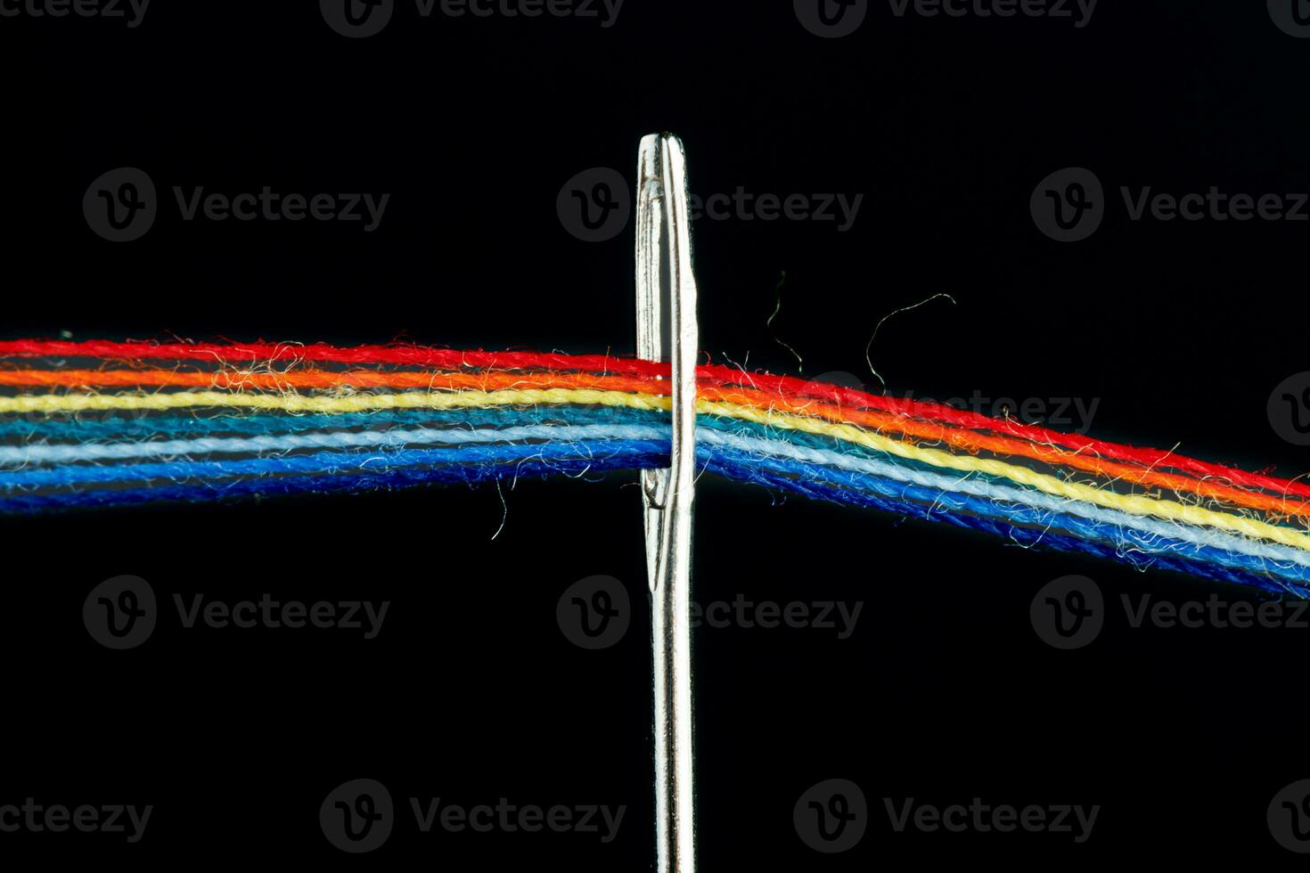 multi-colored threads for sewing in the form of a rainbow pass through an antique needle on a black background photo