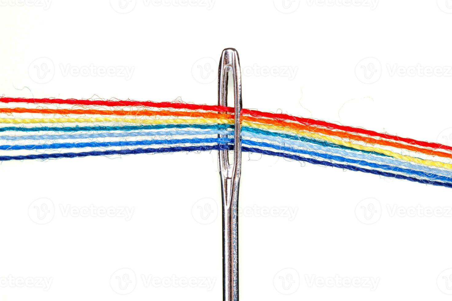 multi-colored threads for sewing in the form of a rainbow pass through an antique needle on a white background photo