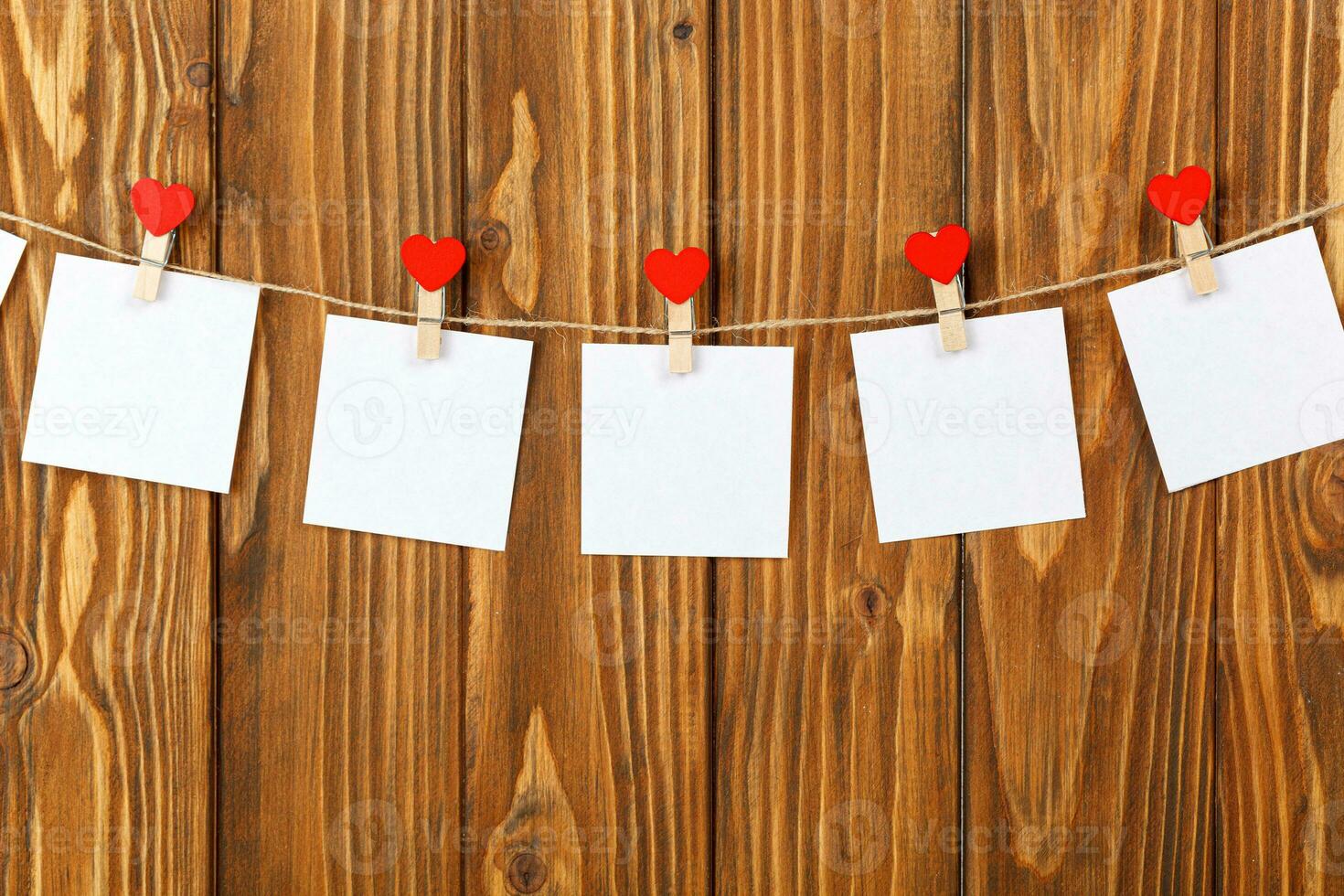 white pieces of paper on clothespins with a heart on a wooden background photo