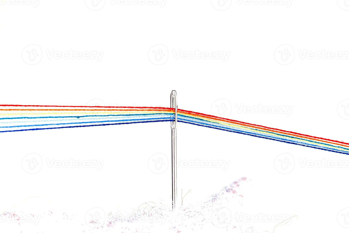 multi-colored threads for sewing in the form of a rainbow pass through an antique needle on a white background photo