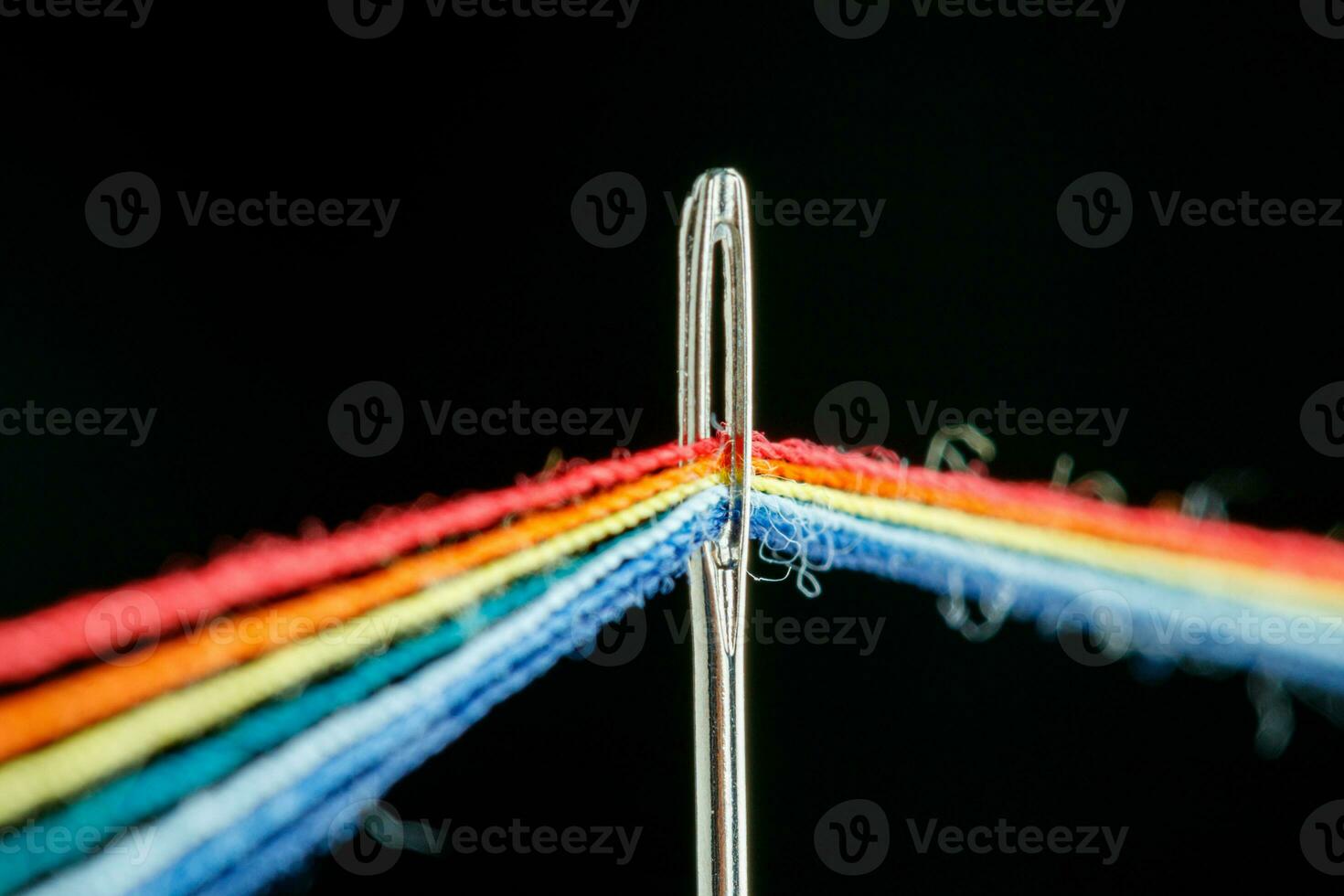 multi-colored threads for sewing in the form of a rainbow pass through an antique needle on a black background photo