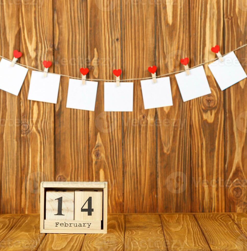 blanco piezas de papel en pinzas para la ropa con un corazón en un de madera fondo, calendario febrero 14 foto