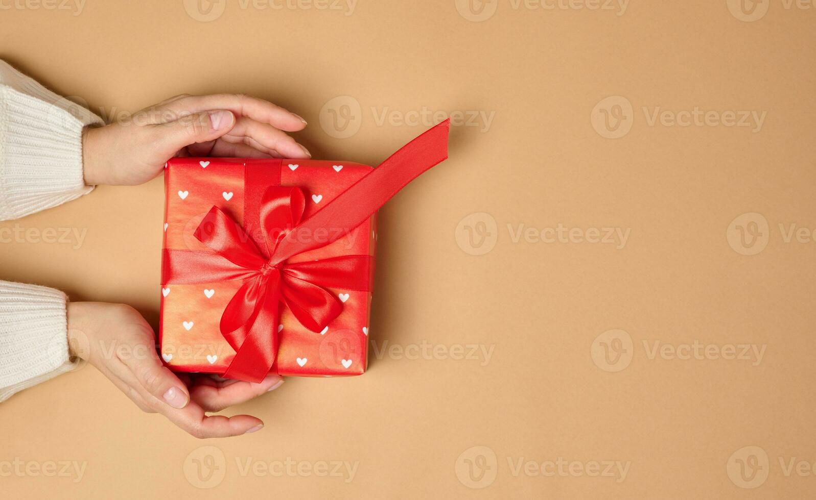 Female hand hold a box wrapped in red paper and tied with a red