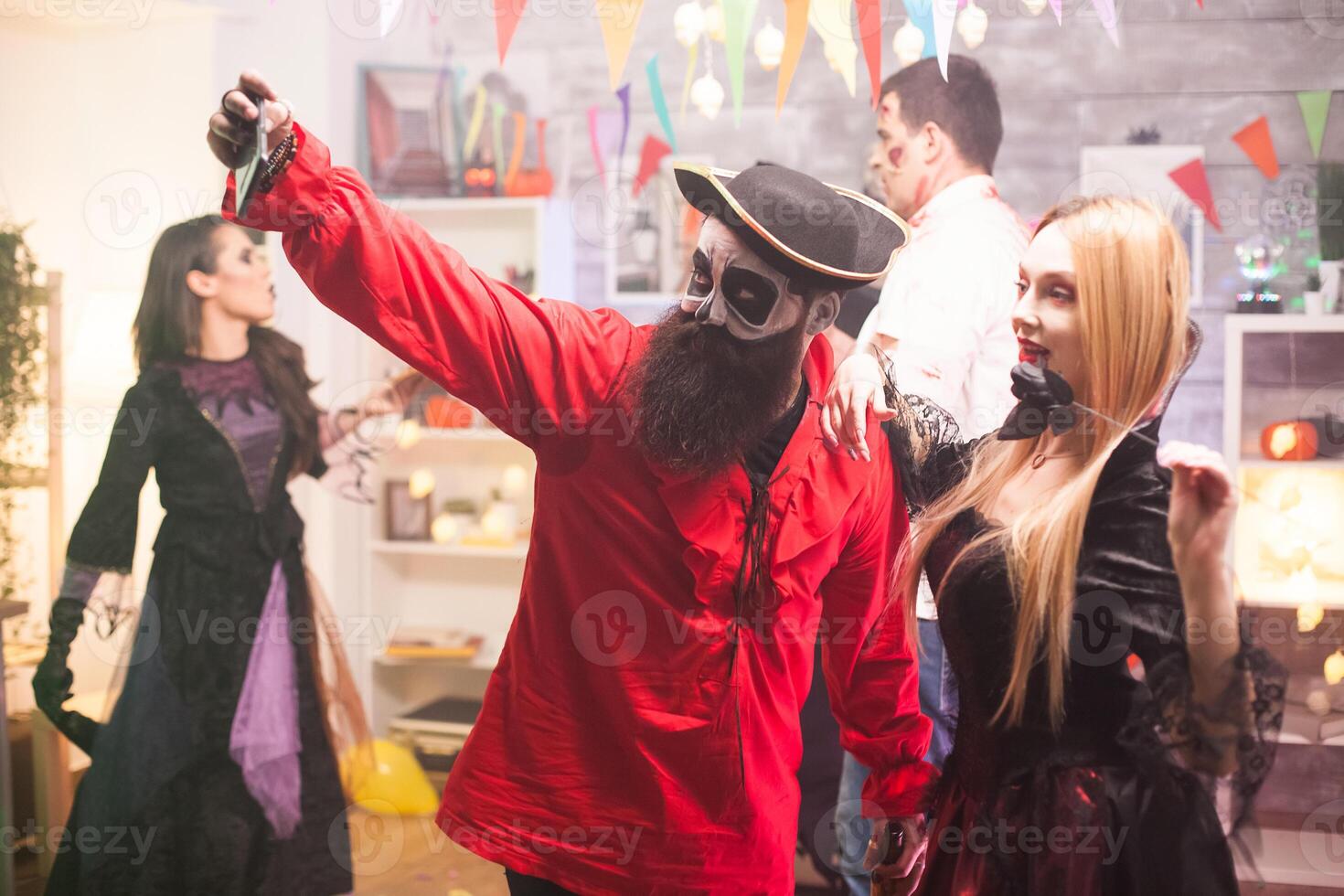 Attractive man and woman dressed up like pirate and vampire taking a selfie at halloween party. photo