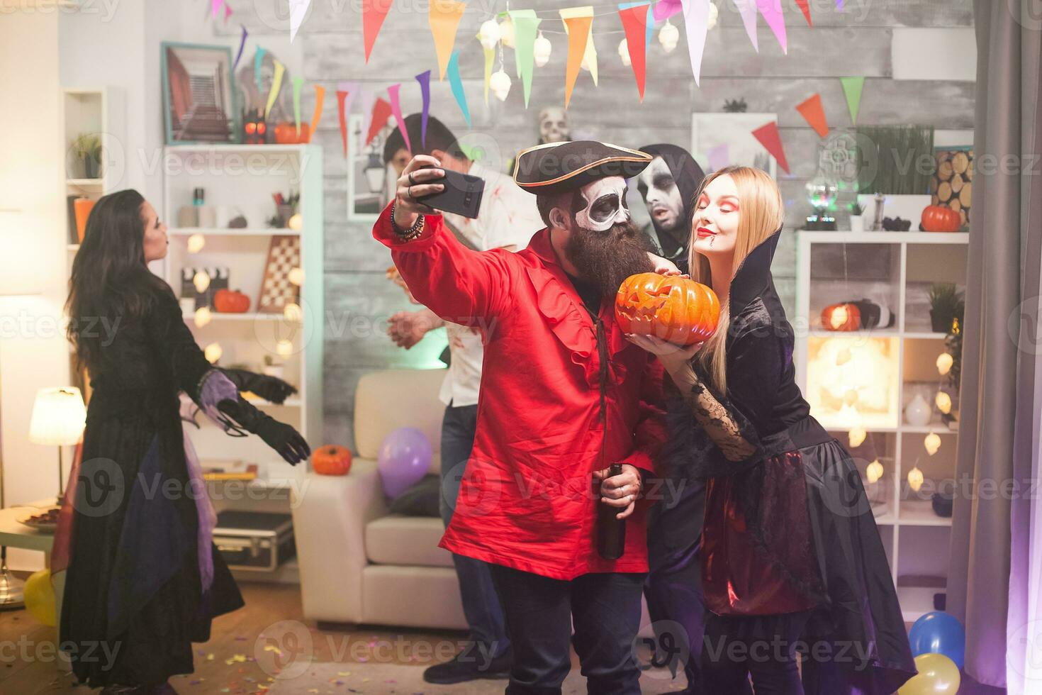 Bearded medieval pirate taking a selfie with beautiful vampire woman at halloween party. Spooky pumpkin. photo