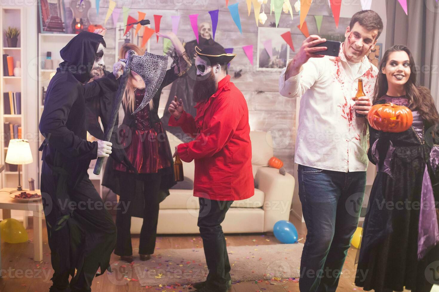 Beautiful witch holding a pumpkin at halloween party while zombie male is taking a selfie. photo