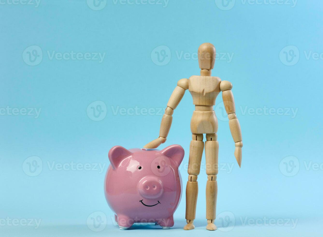 Ceramic pink piggy bank and a wooden puppet doll on a blue background. Concept of increasing income from bank accounts photo