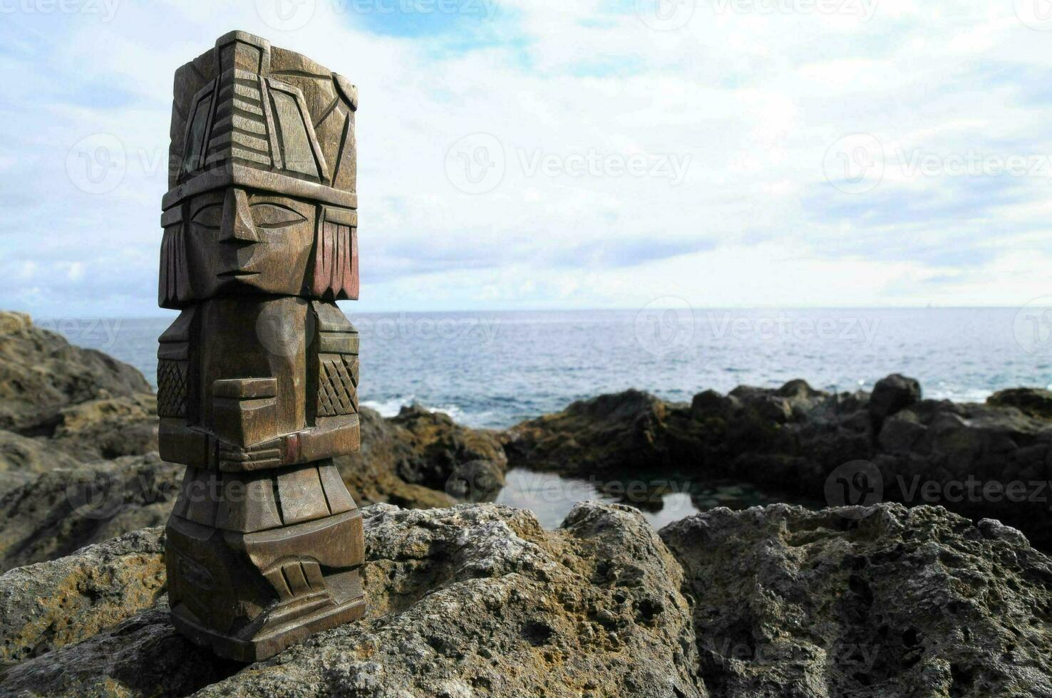 a wooden totem pole stands on the rocks near the ocean photo