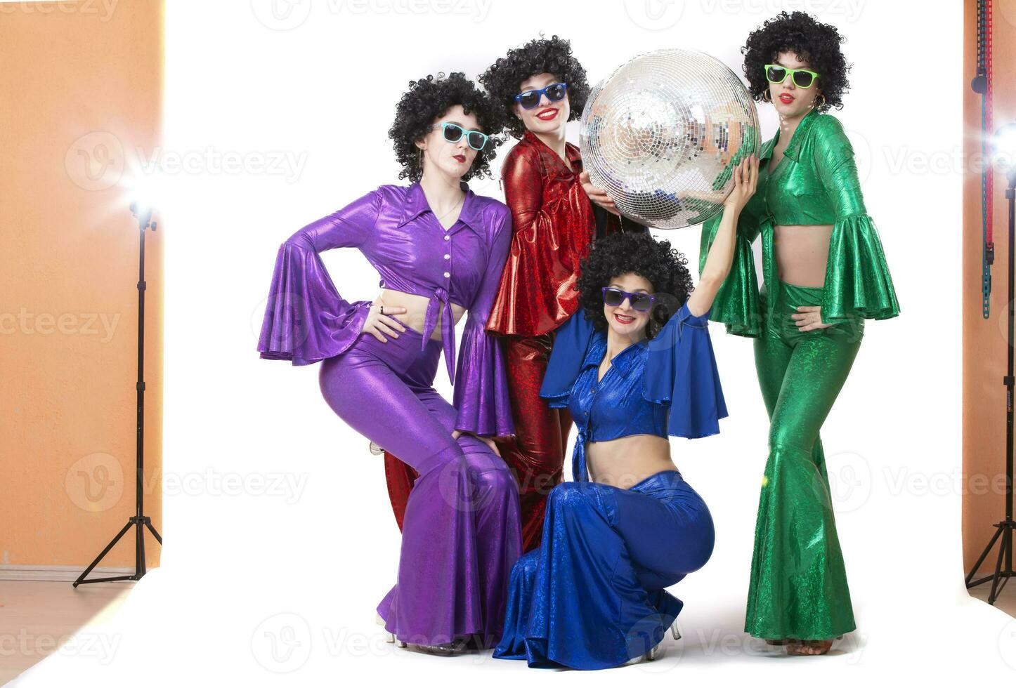 A group of girls in colorful costumes with a disco ball pose in the studio on a white background. photo