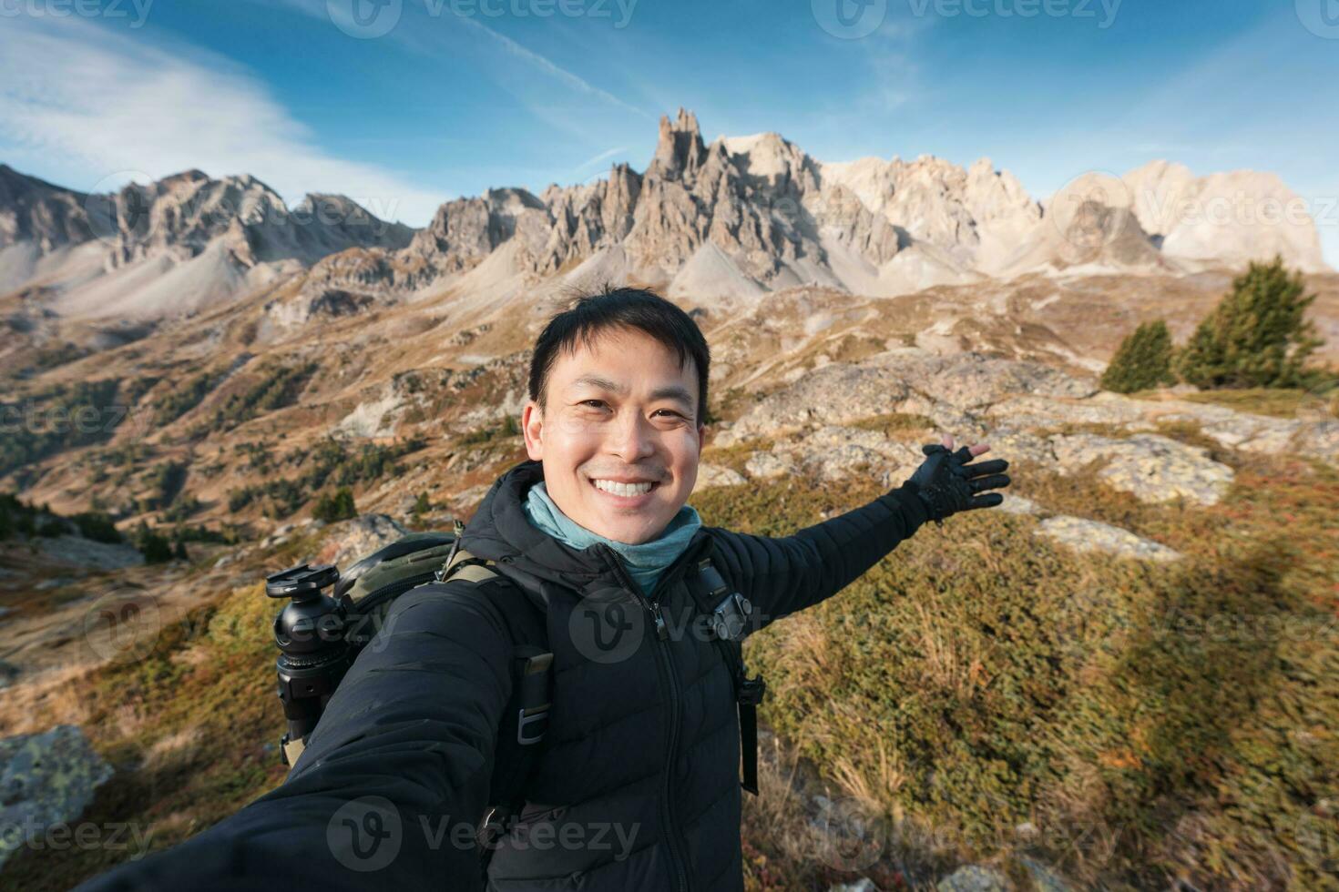 Young asian backpacker man taking selfie on the top of mountain in Valley Claree with iconic mountain in autumn at French Alps, France photo