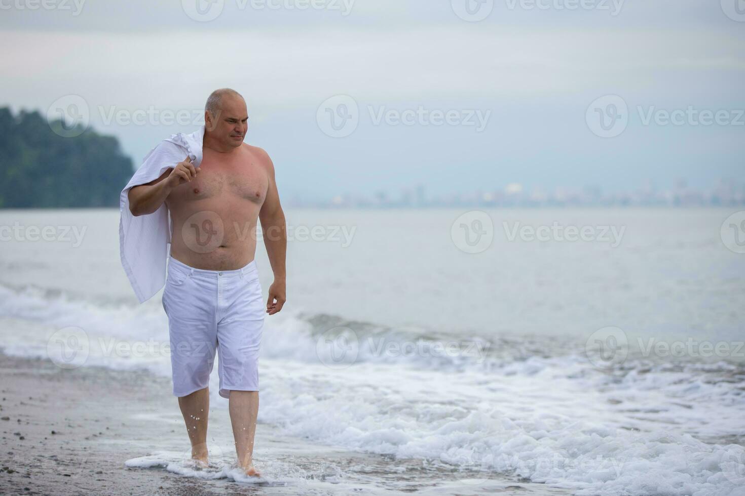An elderly handsome man of athletic build walks along the coast. photo