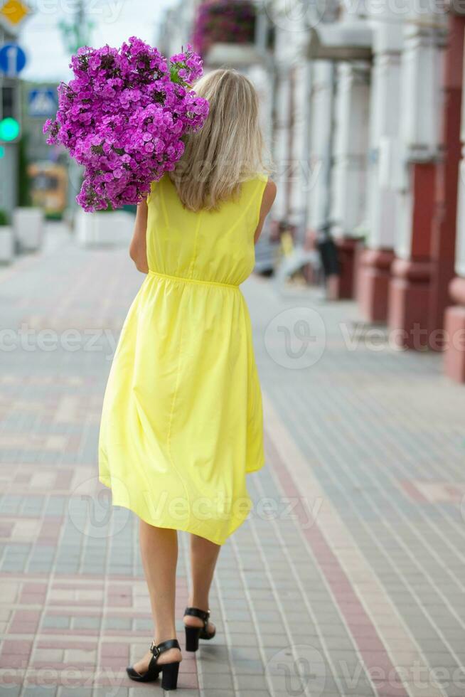 un mujer es caminando abajo el calle con un enorme ramo de flores de flores detrás su. foto