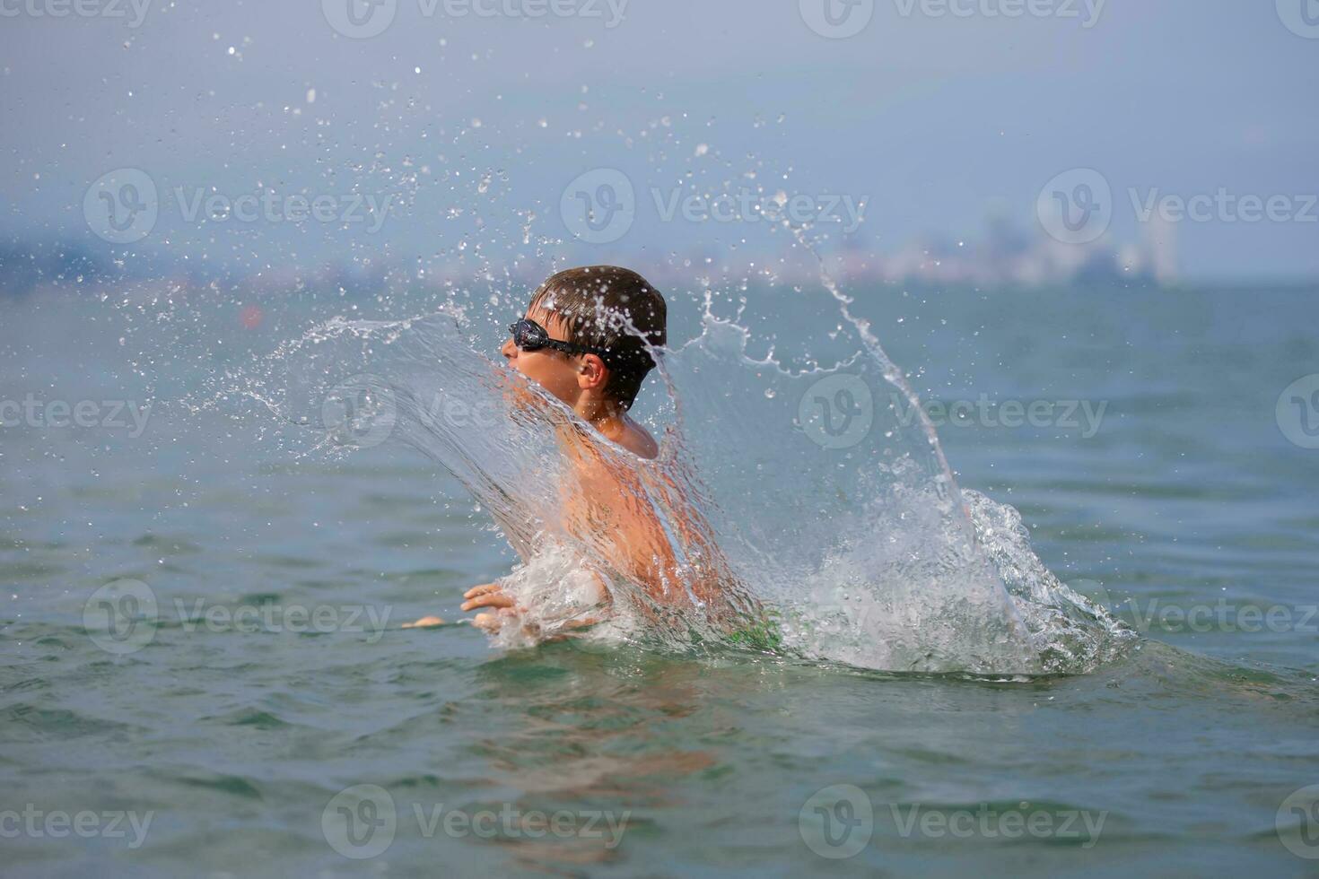 A boy in swimming goggles bathes in the sea, plays with the waves, runs and splashes water. photo