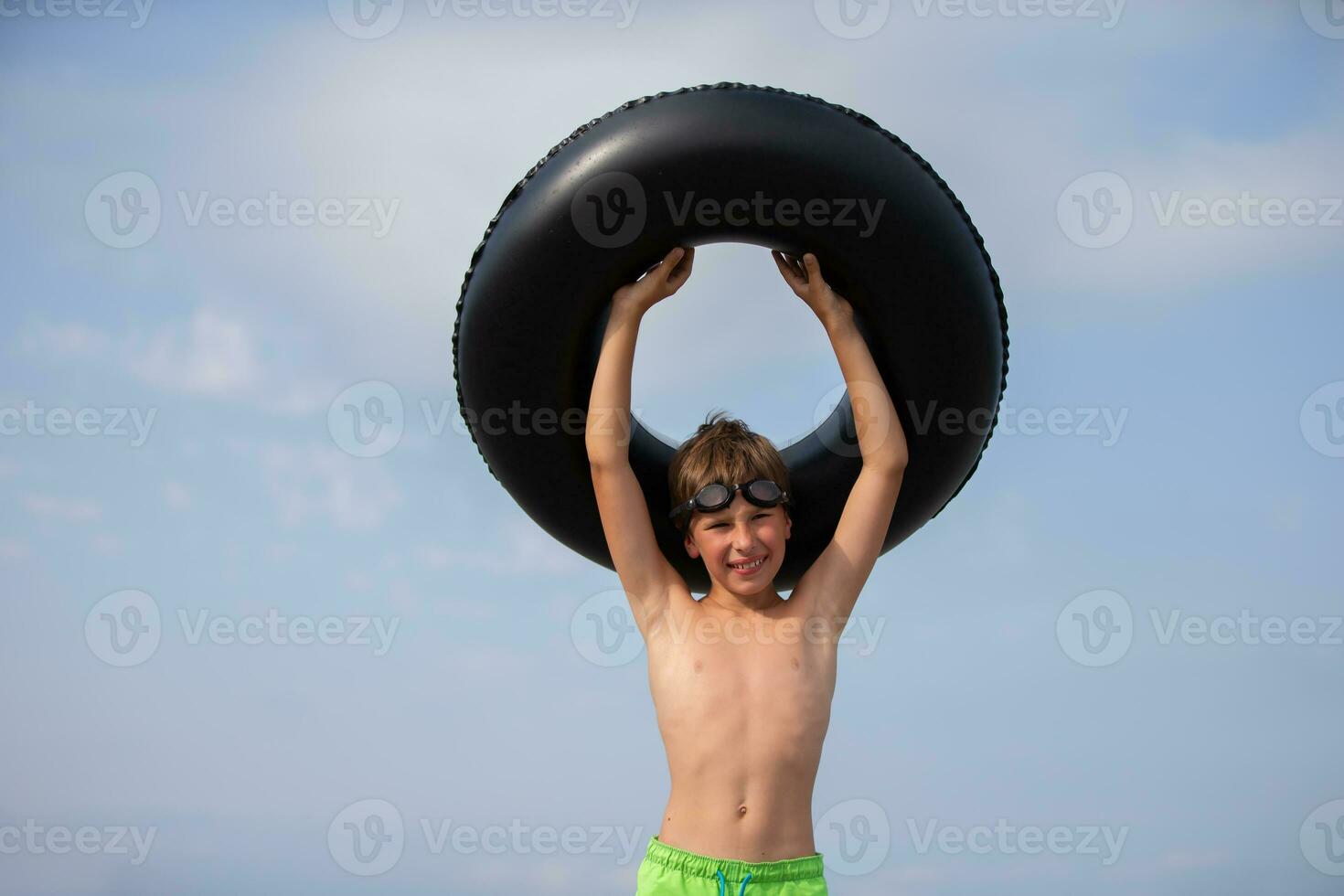 contento chico vistiendo nadando gafas de protección y un inflable nadando boya salvavidas. foto