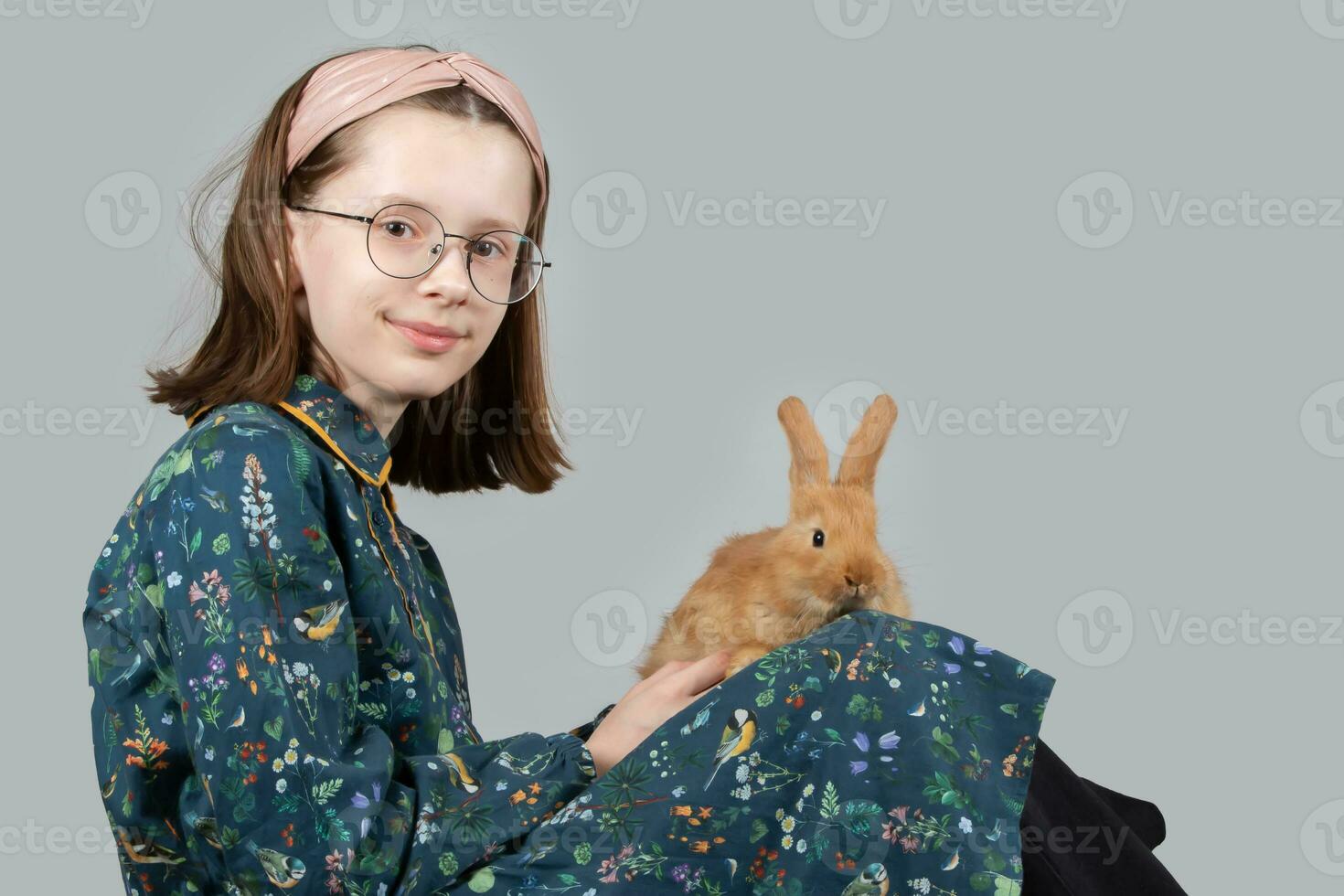 hermosa pequeño niña en lentes obras de teatro con un rojo Conejo en un gris antecedentes. foto