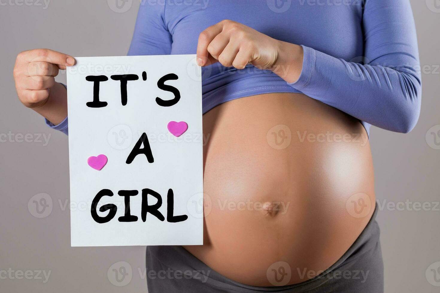 Image of close up stomach of pregnant woman holding paper with text it's a girl on gray background. photo