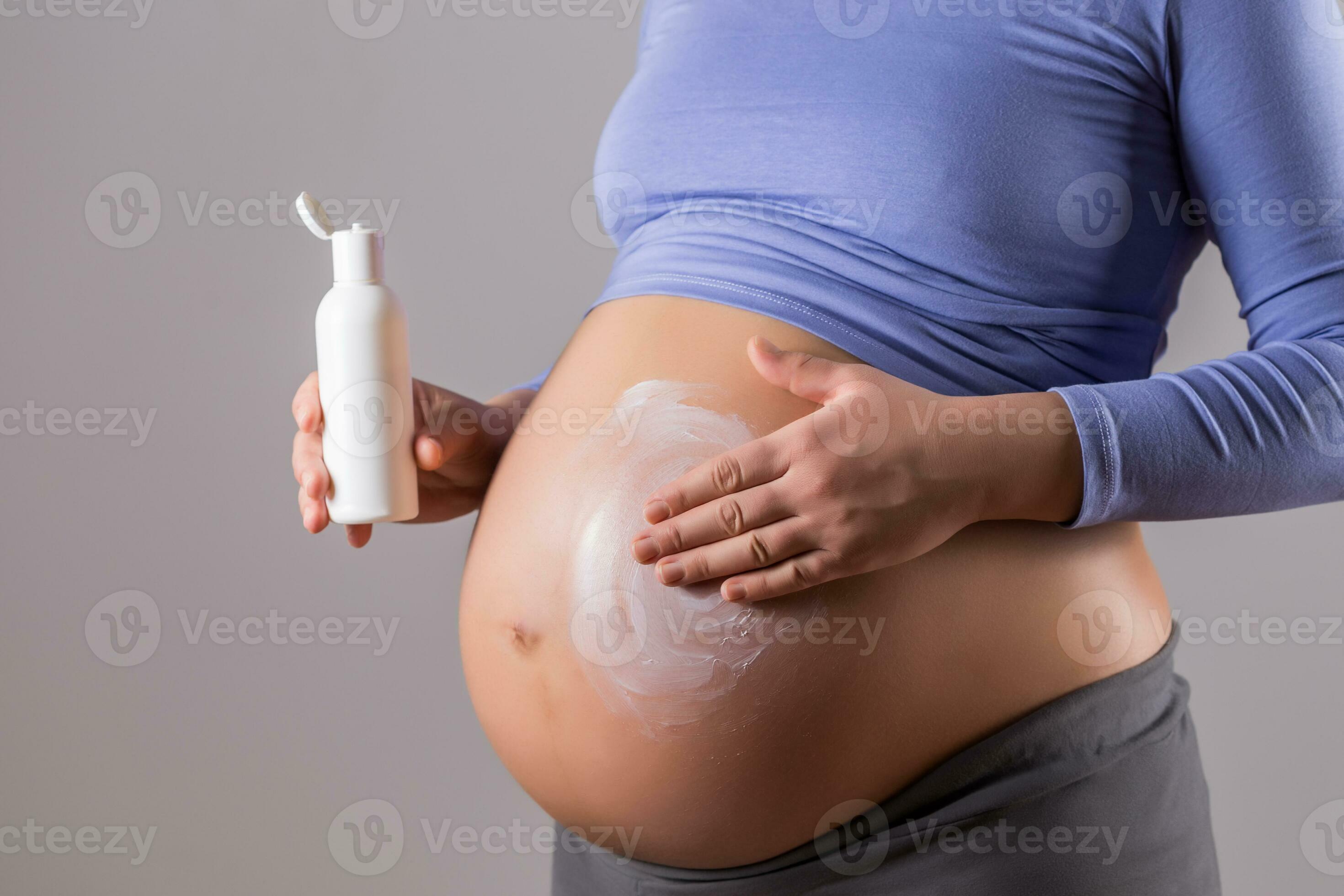 Image of pregnant woman applying moisturizer on her stomach on gray
