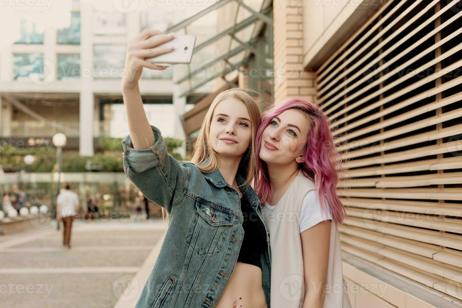 Two happy girlfriends taking photo with their smartphone in the city