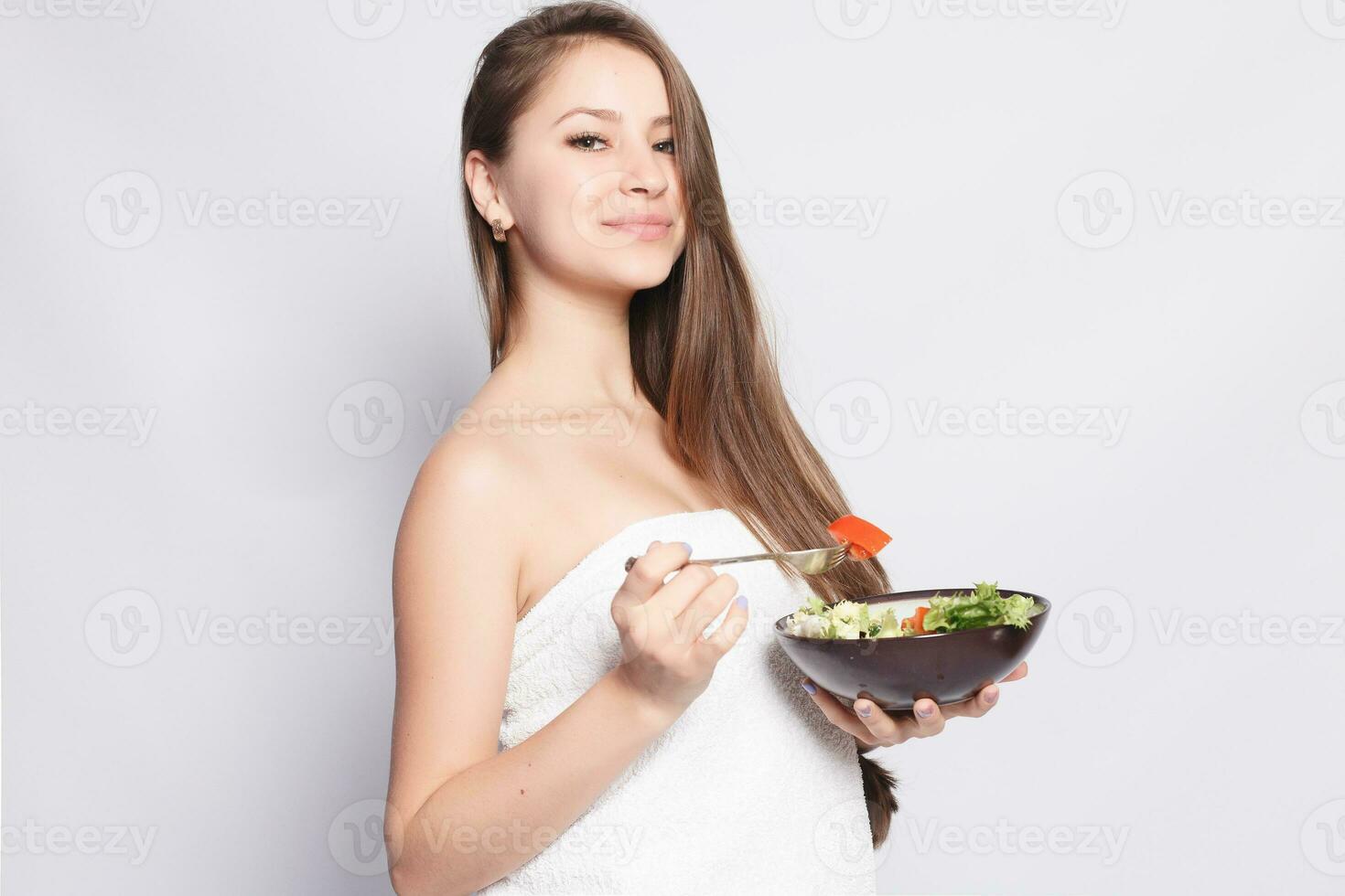 Beautiful brunette girl in towel eating fresh salad and smiling photo