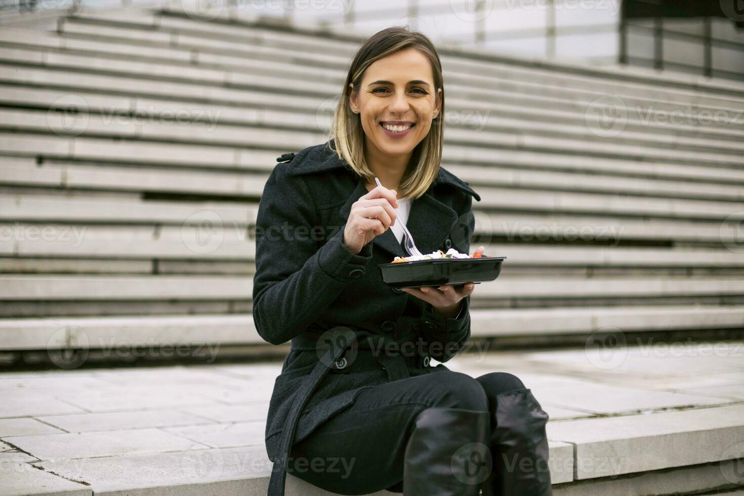 hermosa mujer de negocios disfruta descansando en un almuerzo descanso mientras sentado en el escalera en el ciudad. foto