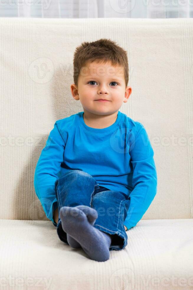 Cute little boy is sitting on sofa. photo