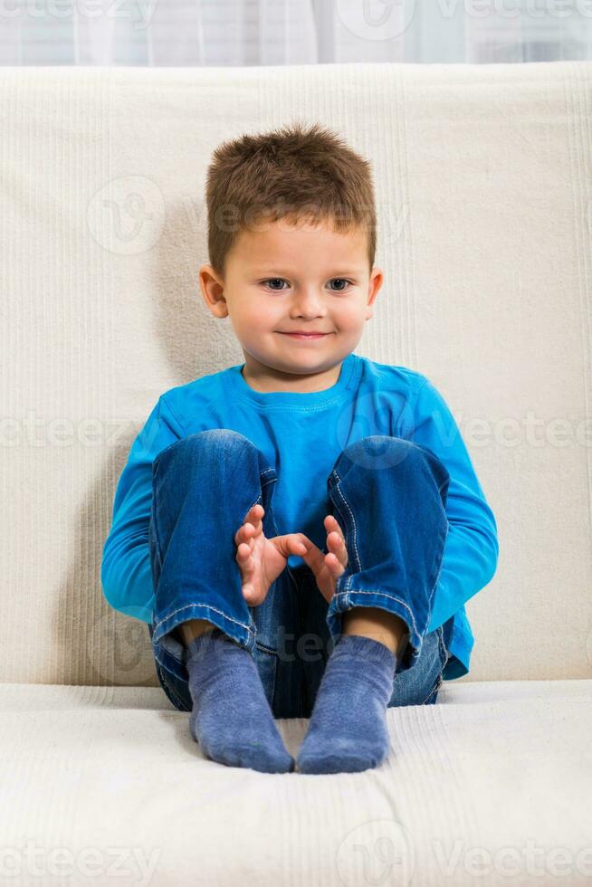 Cute little boy is sitting on sofa. photo