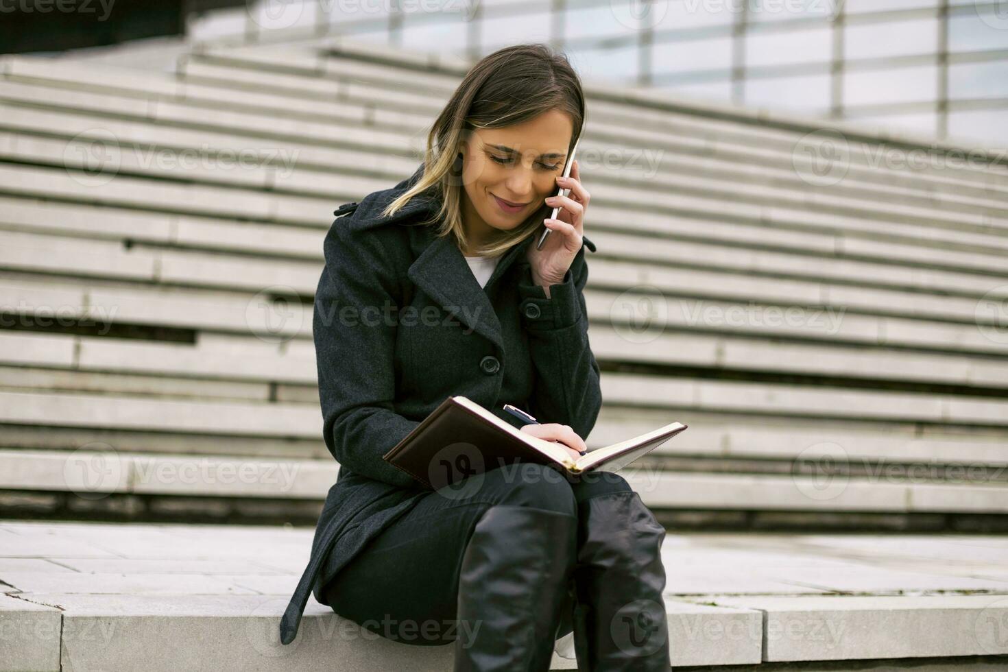 Businesswoman using phone and personal organizer while working outdoor. photo