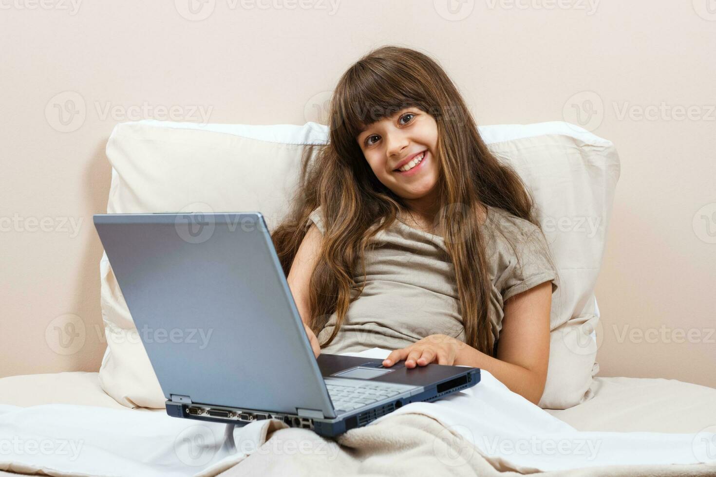 Little girl using laptop in bed photo