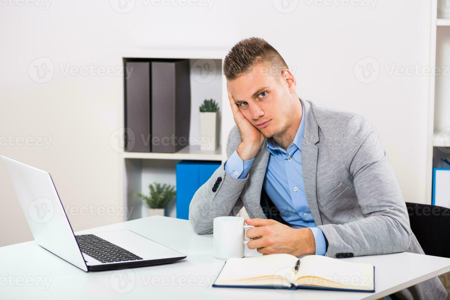 Exhausted businessman drinking coffee at his office. photo