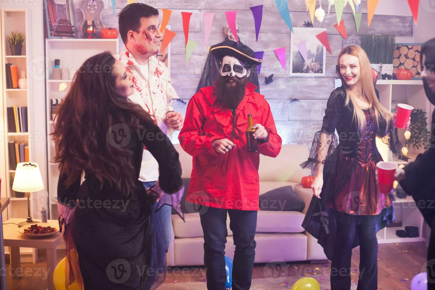 Cheerful young woman dressed up like a vampire with bloody lips at halloween celebration with her funny friends. photo