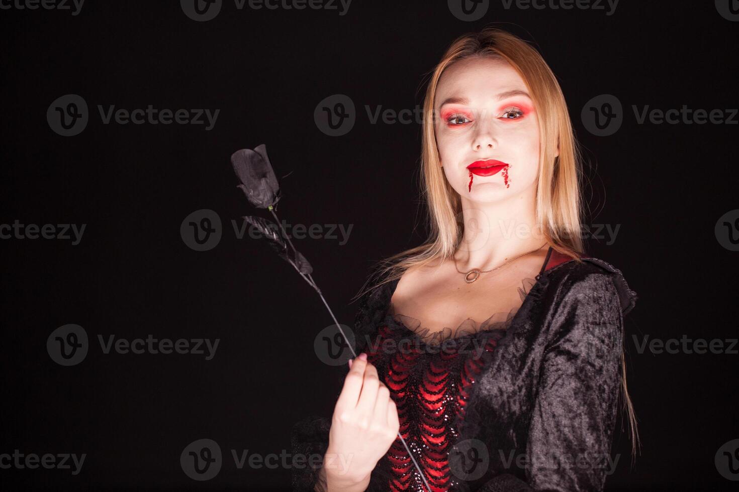 caucásico vampiro mujer con sangriento labios terminado negro antecedentes. Víspera de Todos los Santos traje. foto