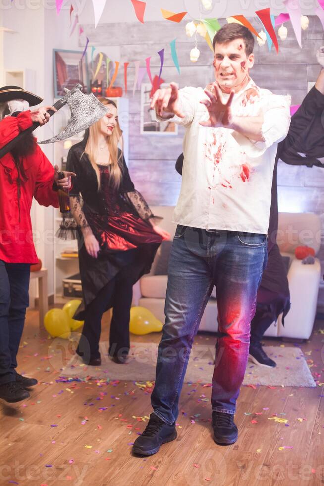 Man wearing a zombie costume with creepy expression at halloween celebration with his friends. photo