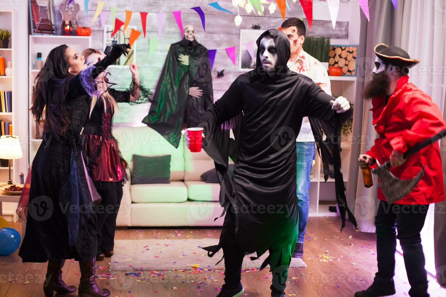 Cheerful man dressed up like a grim reaper with dancing moves at halloween party. photo