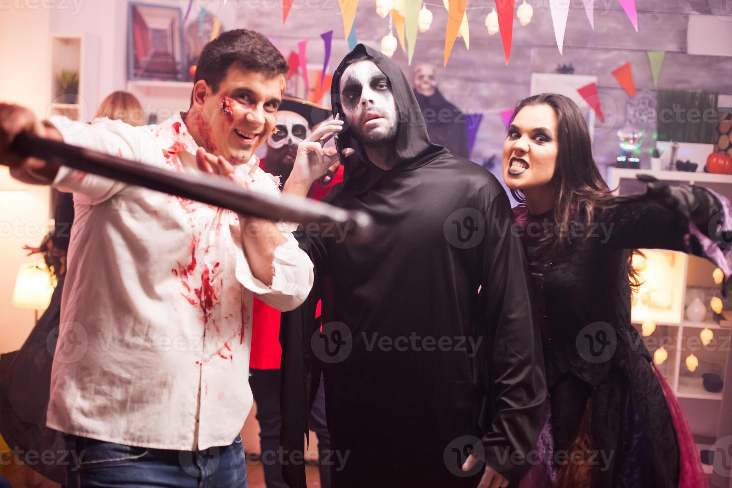 Group of friends in spooky costumes celebrating halloween. Grim reaper using smartphone. photo