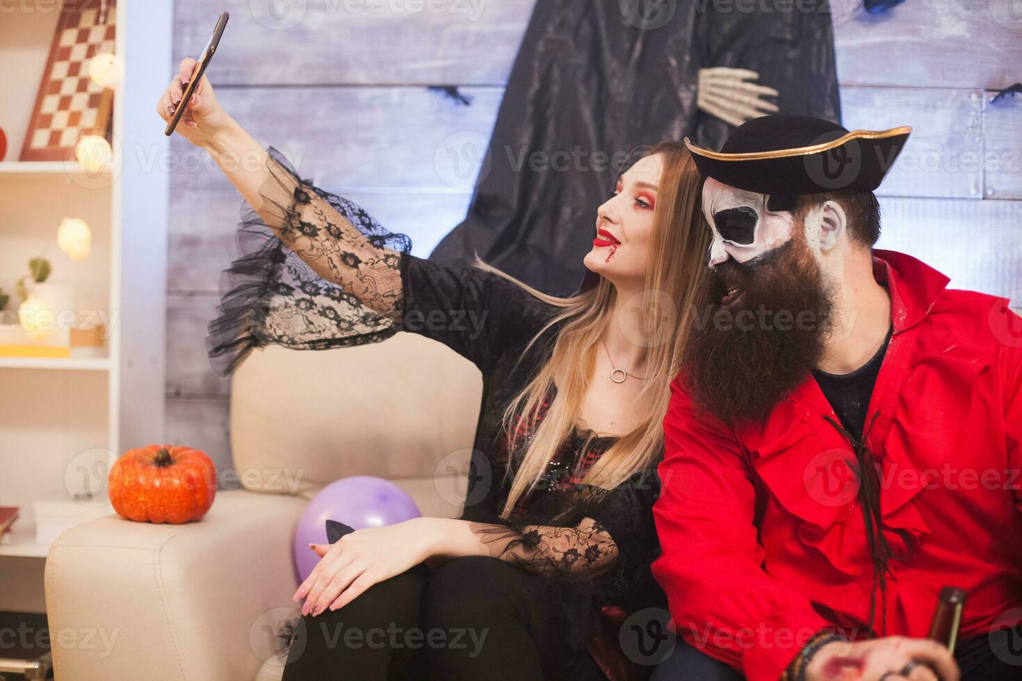 Medieval pirate winking while vampire woman taking a selfie at halloween party. photo