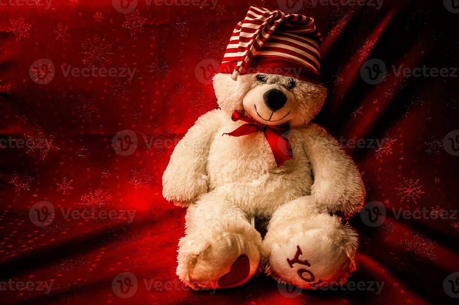 White soft plush toy baby little teddy bear in a red bow-tie sits on a background of burgundy curtain photo