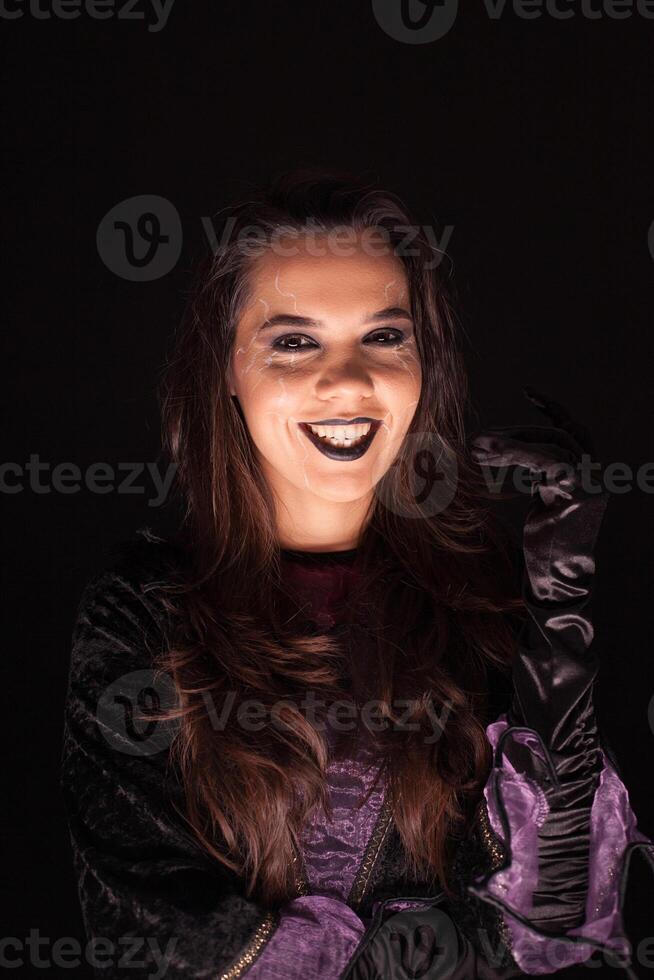 Beautiful woman dressed up like a witch having a scary smile over black background. photo